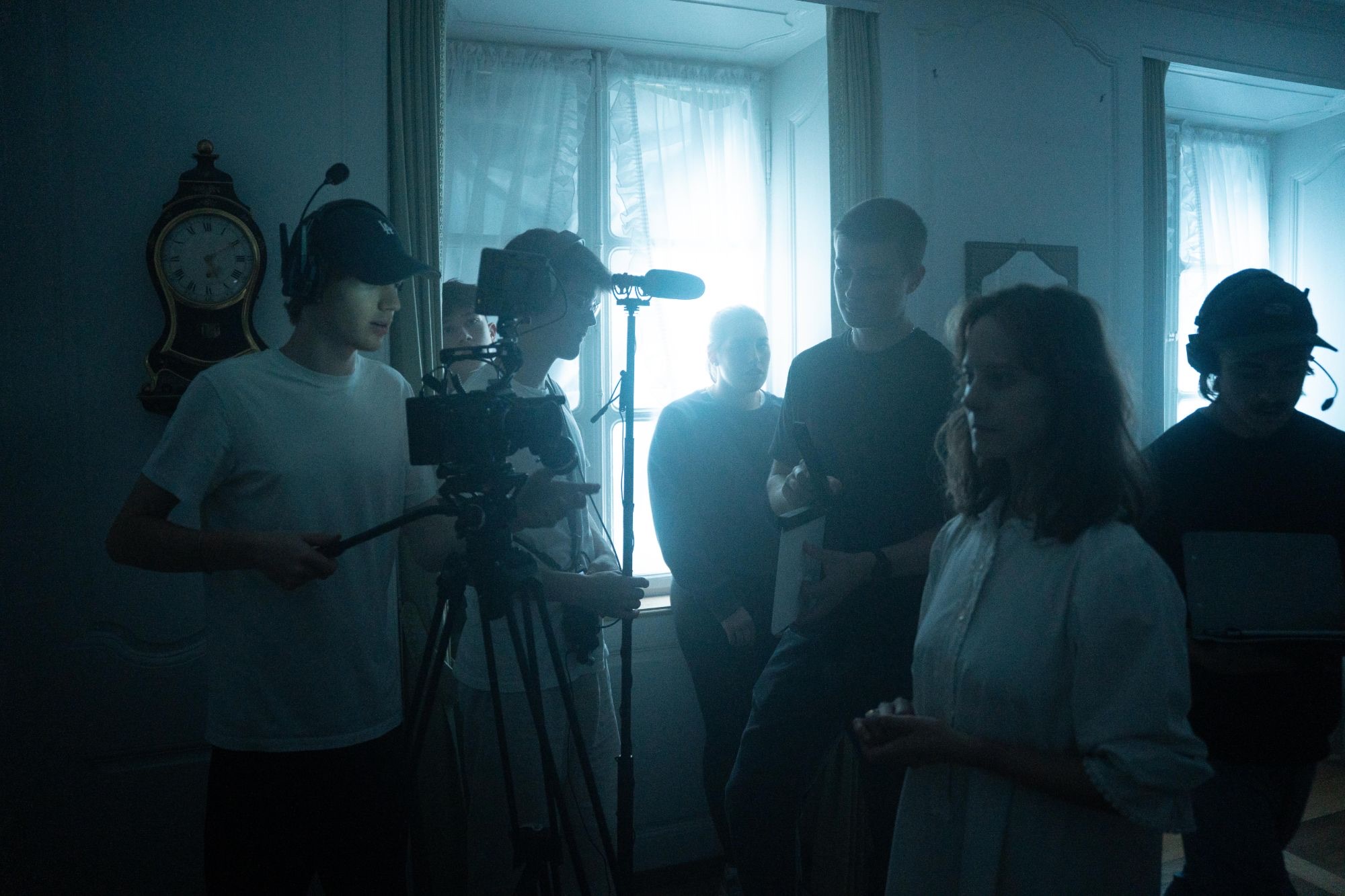 Crew mit Kamera, Tonangel und Klappe im Gegenlicht eines Fensters