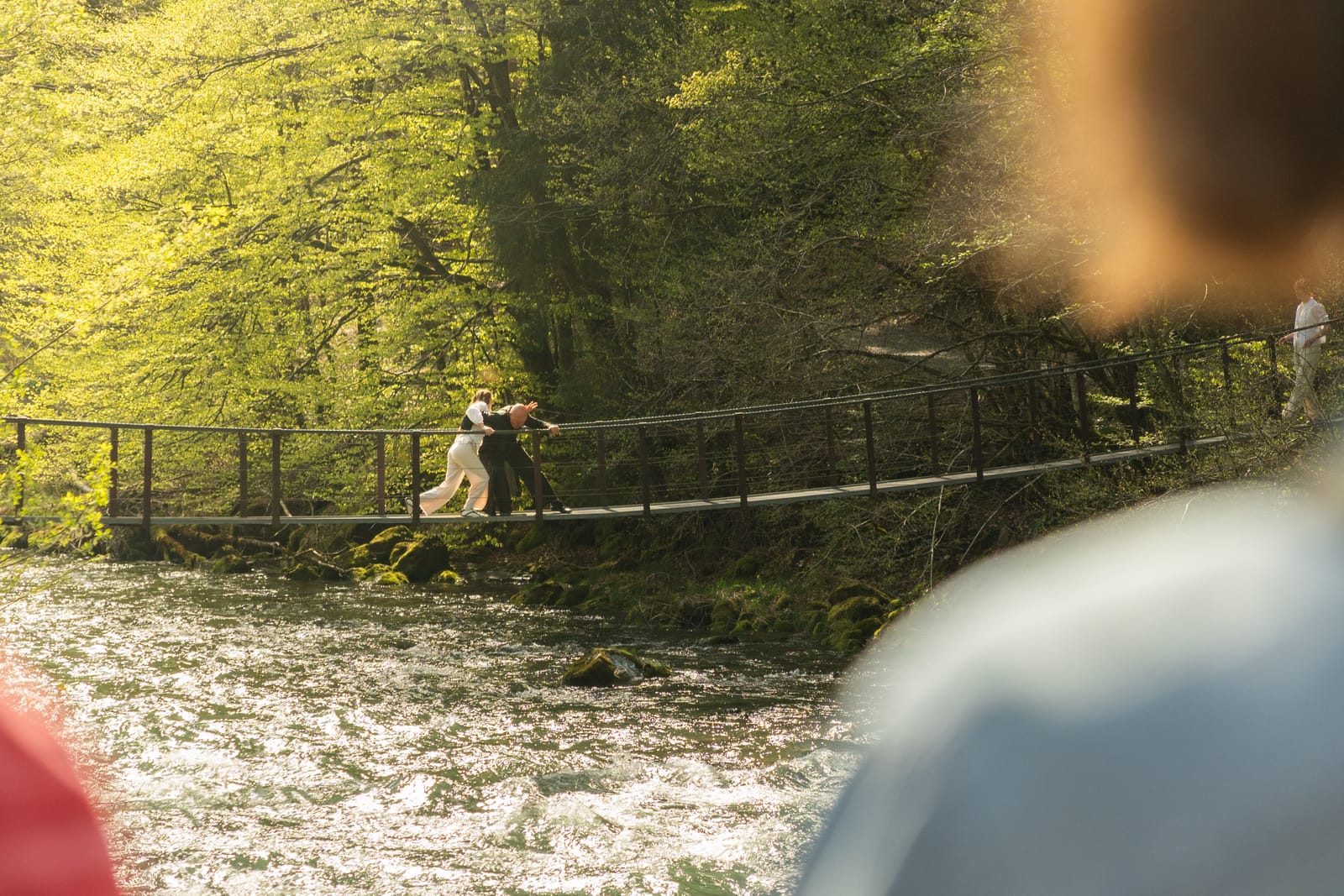Zwei Figuren auf einer Hängebrücke über einem Bach